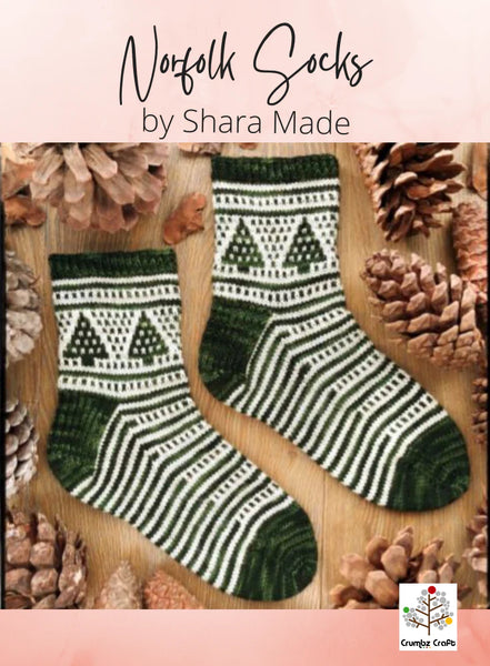 Pair of green and white patterned socks on a wooden surface with pine cones.